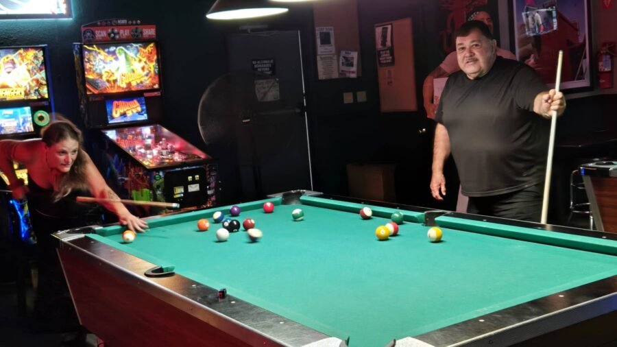 Two people playing pool by the arcade machines